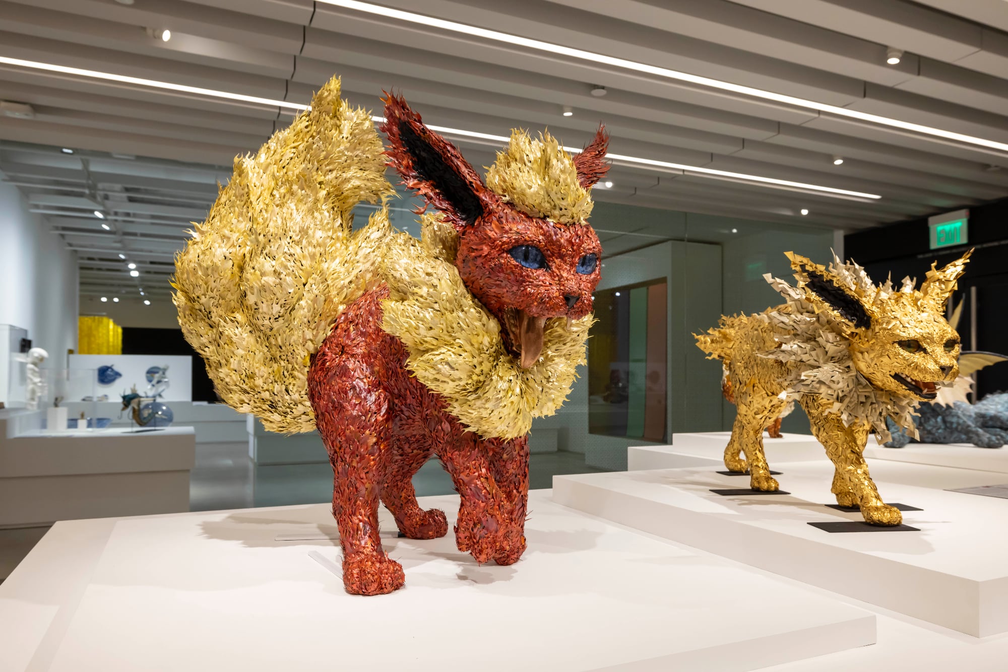 two cat like animal sculptures covered in small metal layers in gold and red