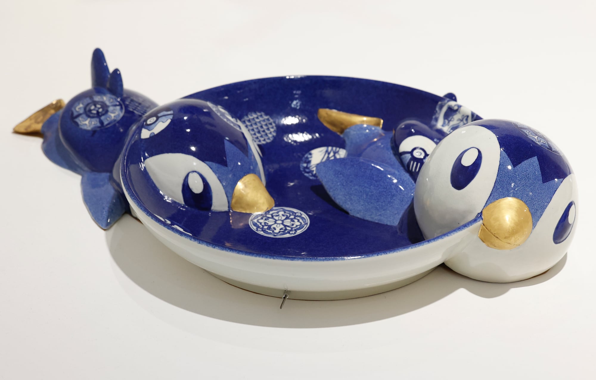 a ceramic plate in blue and white with bird characters emerging from the sides