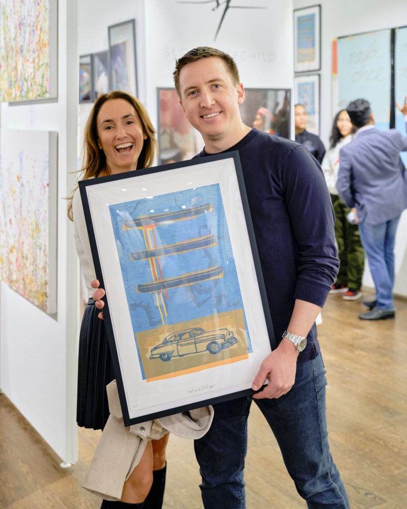 Two visitors to Affordable Art Fair holding up an abstract artwork.