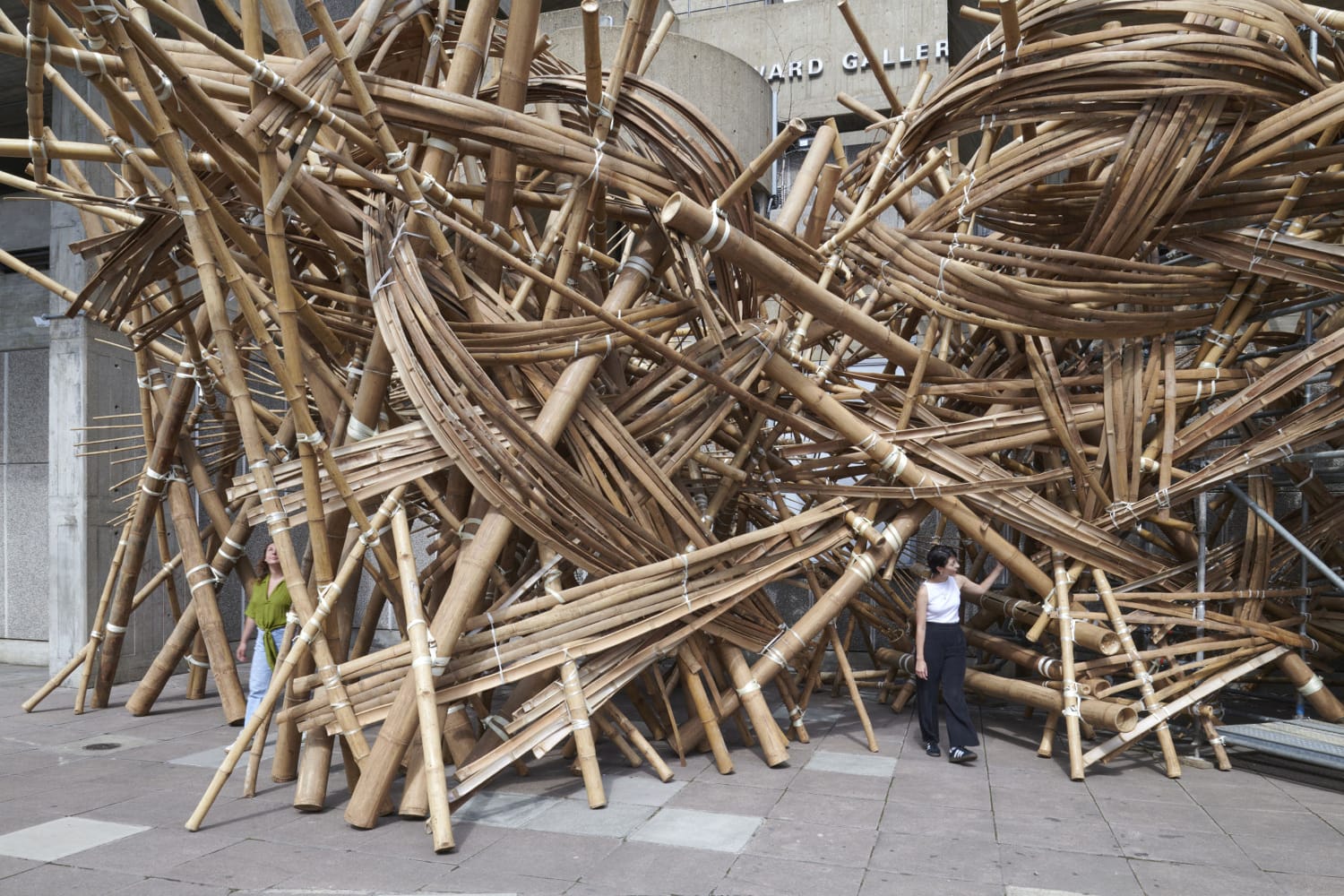 a person stands in a large bamboo structure on the sidewalk