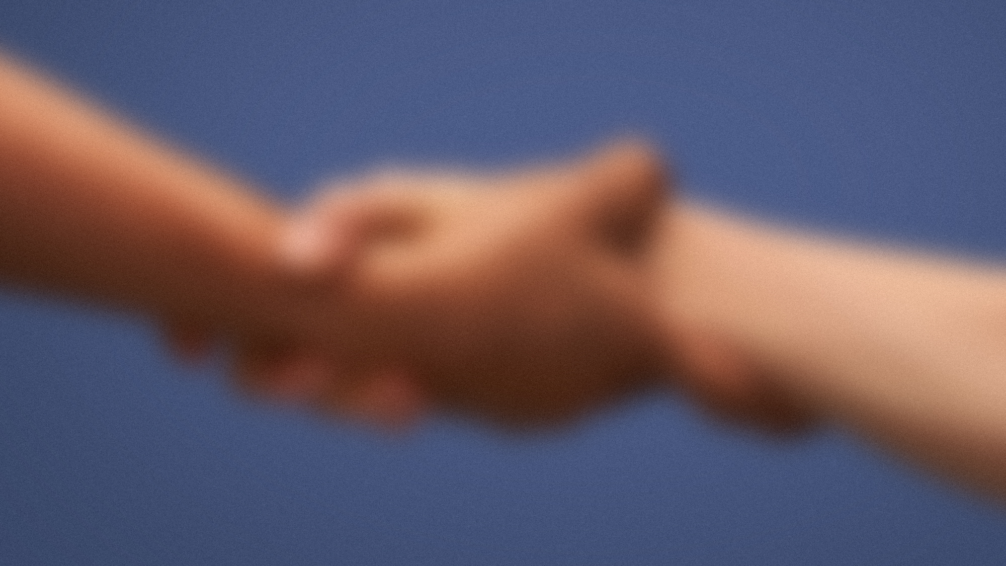 A blurred image shows one person's hand clasping another's.
